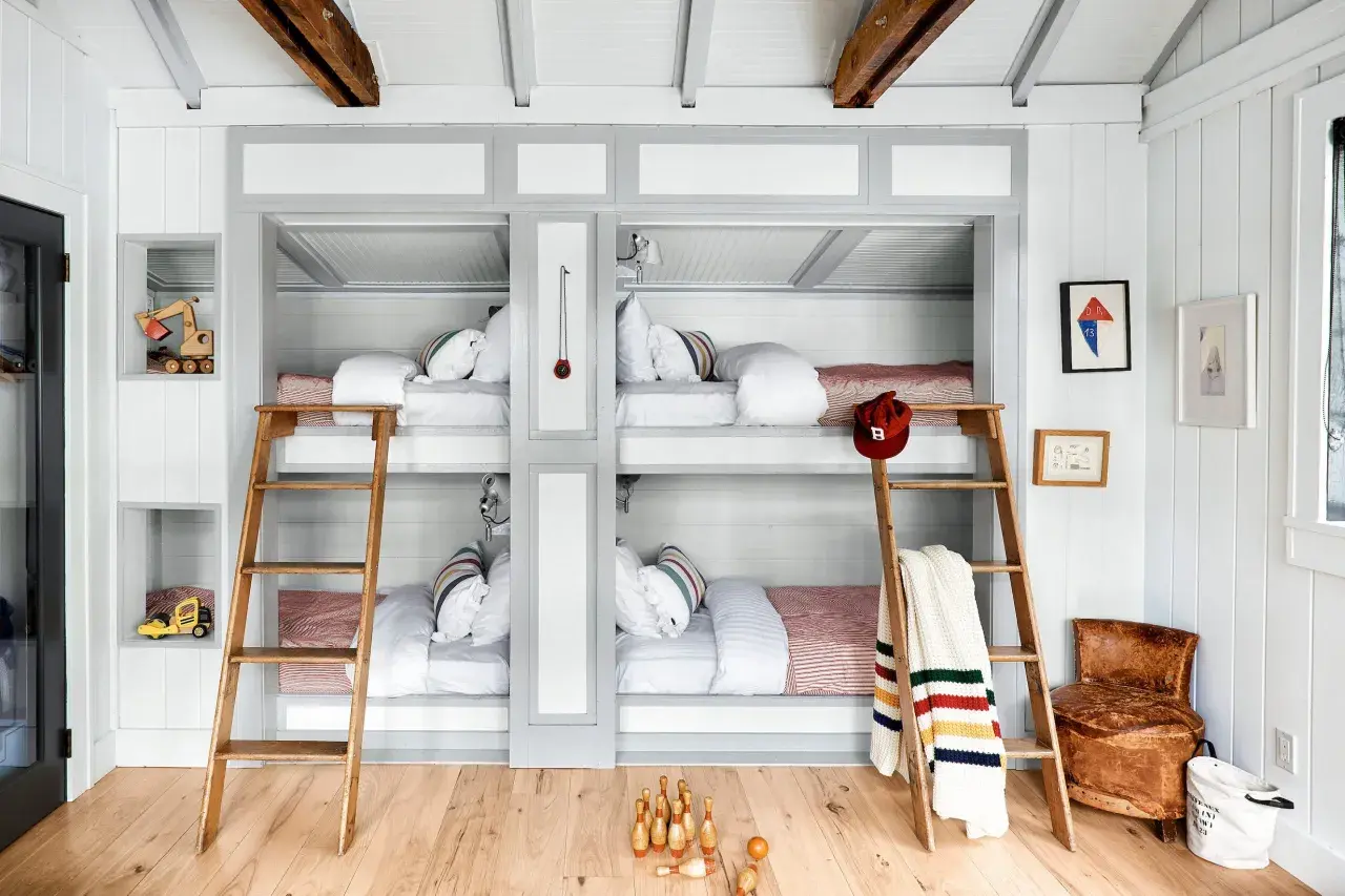 A cozy built in bunk room with four beds, wooden ladders, and playful decor like toy excavators and bowling pins.