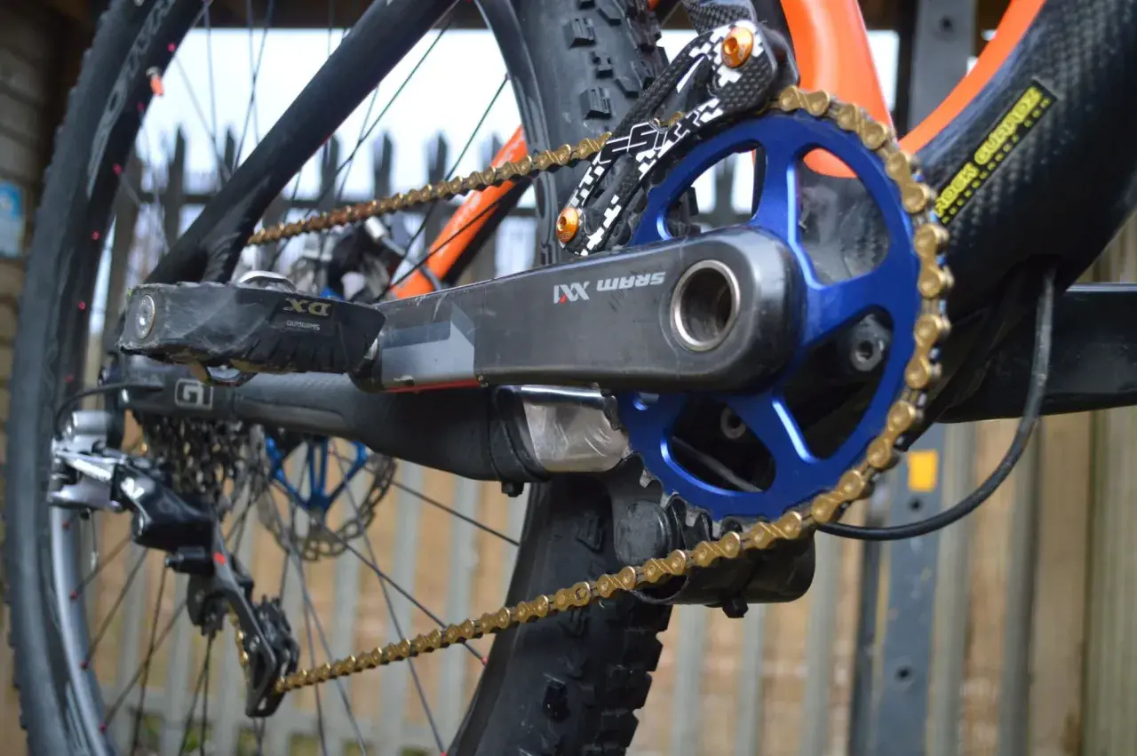 Close-up of a mountain bike's drivetrain, featuring a SRAM XX1 chain, blue chainring, and black crank arm.