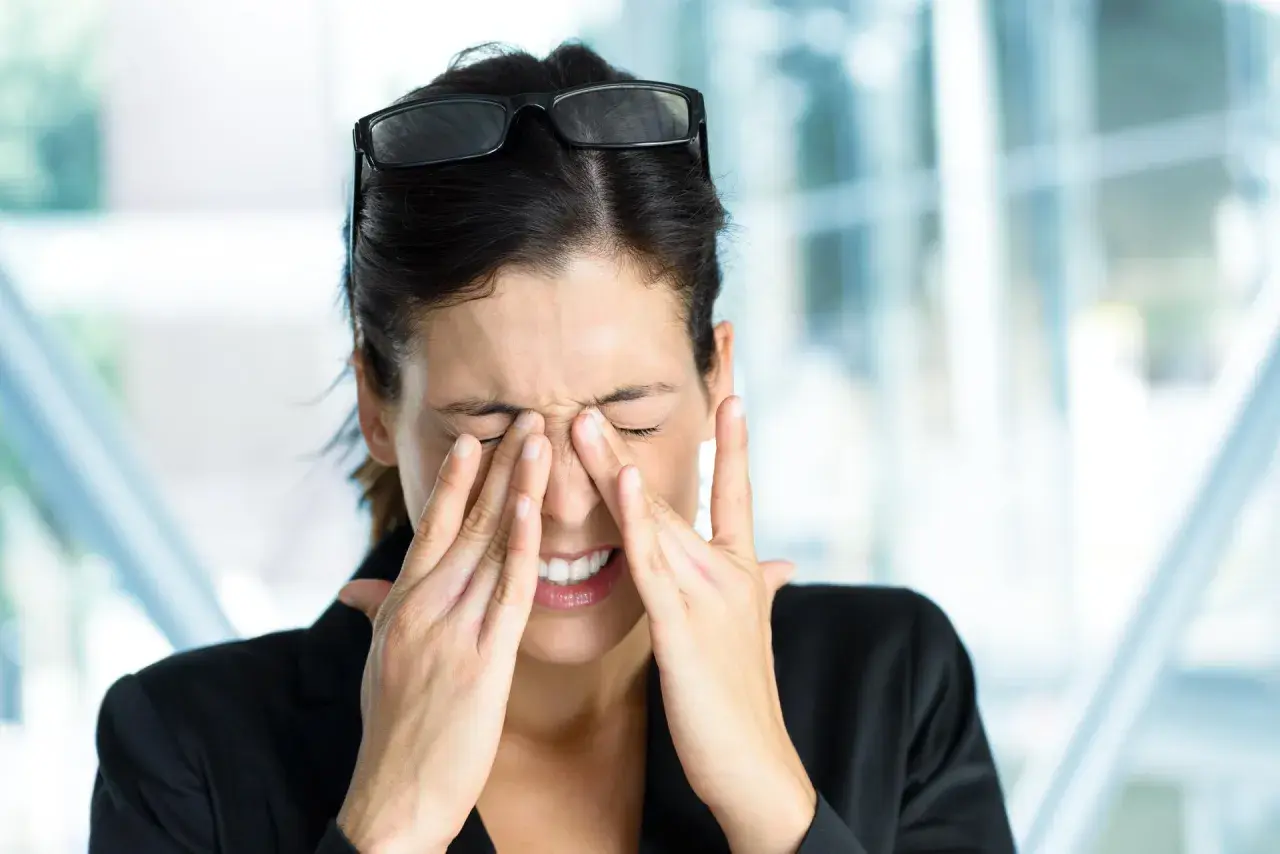 Kobieta z zespołem Sjogrena, zamyka oczy i masuje nos, cierpiąc z powodu suchości i bólu.
