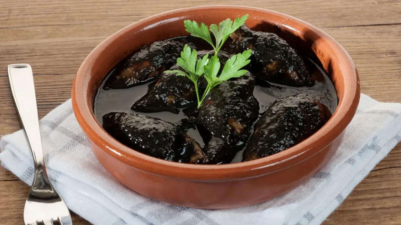 Chipirones en salsa negra, un plato tradicional servido en cazuela de barro, con perejil fresco y un tenedor al lado.