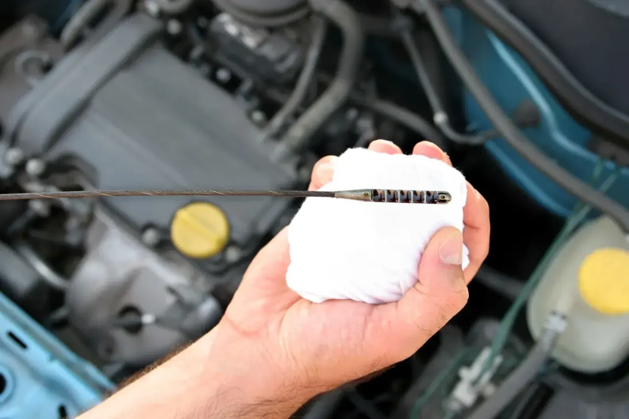 Mano limpiando la varilla del nivel de aceite en el motor. El aceite está entre las marcas de mínimo y máximo.