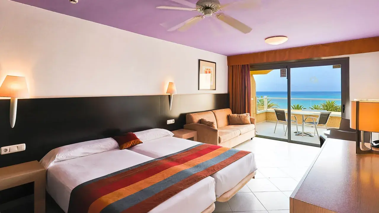 Gemütliches Zimmer im SBH Monica Beach Resort mit Meerblick. Zwei Betten, Sofa und Balkon laden zum Entspannen ein.
