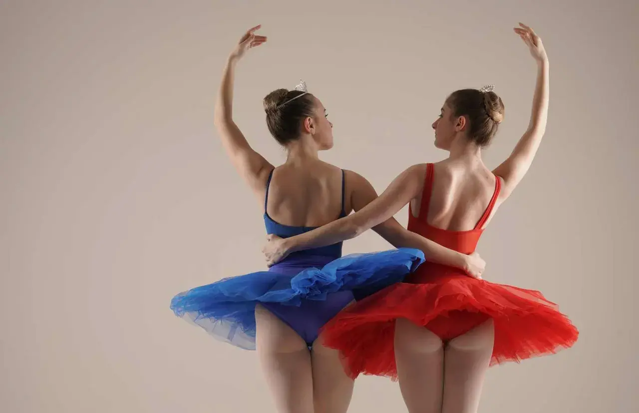 Due ballerine, una in blu e una in rosso, con tutù e diademi, si abbracciano durante un corso di danza per bambini.