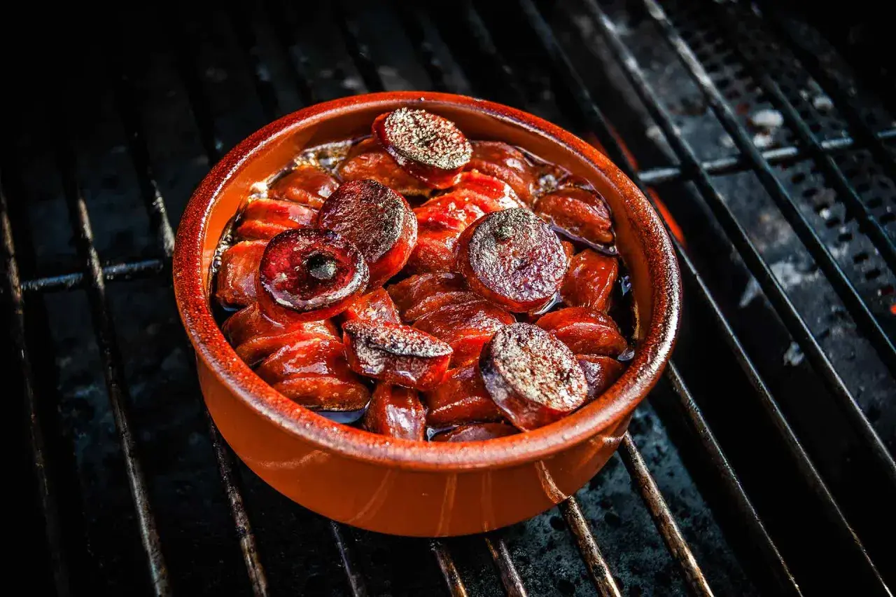 Heiß gegrillte Chorizo-Tapas in einer Tonschale, die auf einem Grillrost brutzeln.