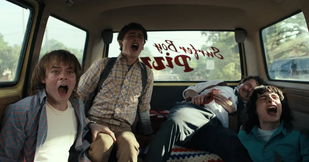 Czterech przerażonych przyjaciół z Stranger Things 4 krzyczy w vanie, gdy przejeżdżają obok Surfer Boy Pizza.