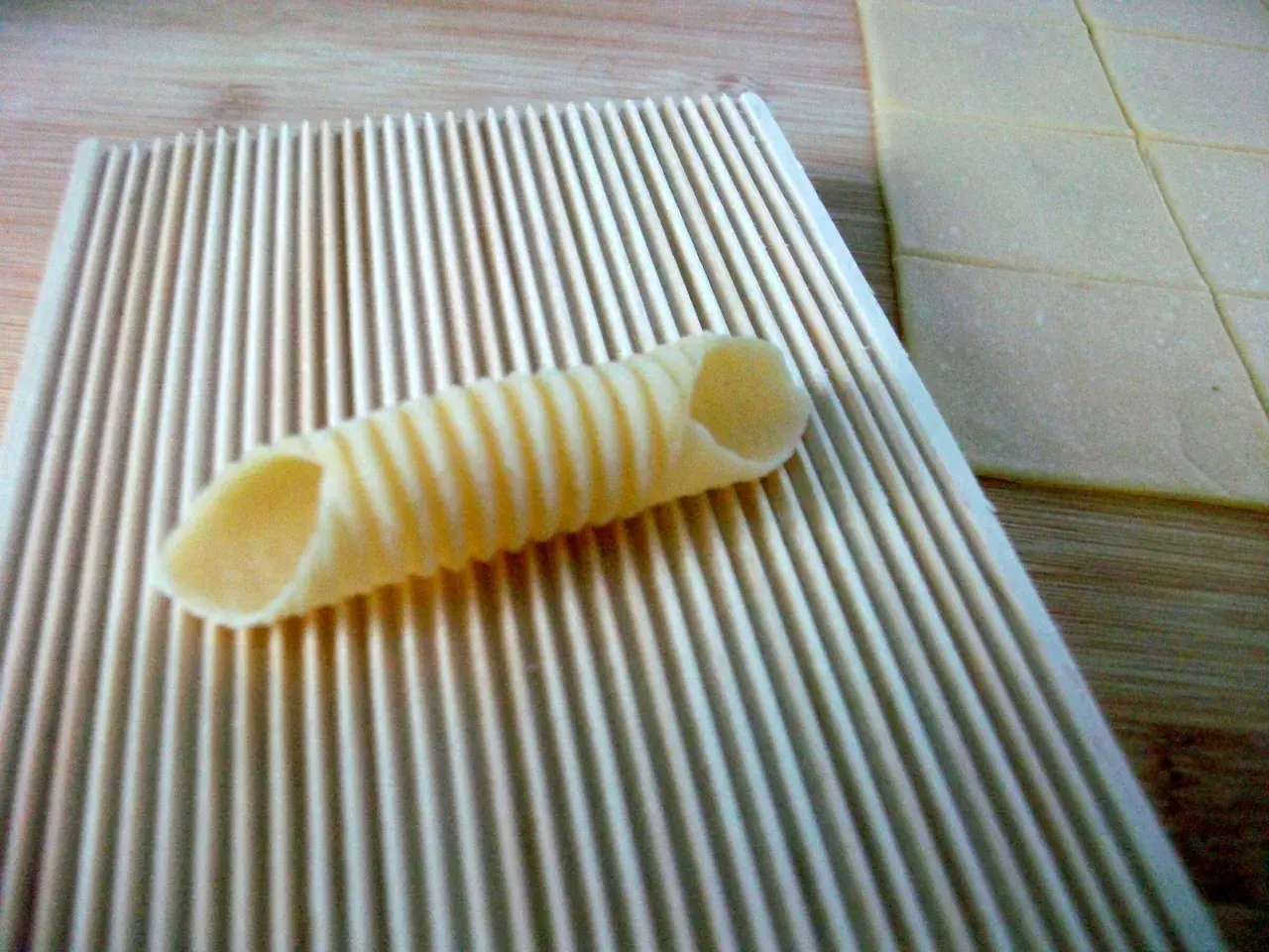 Frische Pasta selbst machen ohne Maschine: Ein geriffeltes Werkzeug formt Teig zu Röhren. Daneben liegen Teigplatten.