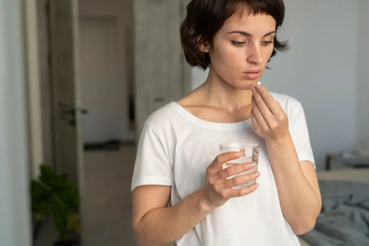 Mujer toma pastilla con agua, pensando en cuando tomar probióticos con antibióticos para cuidar su salud intestinal.