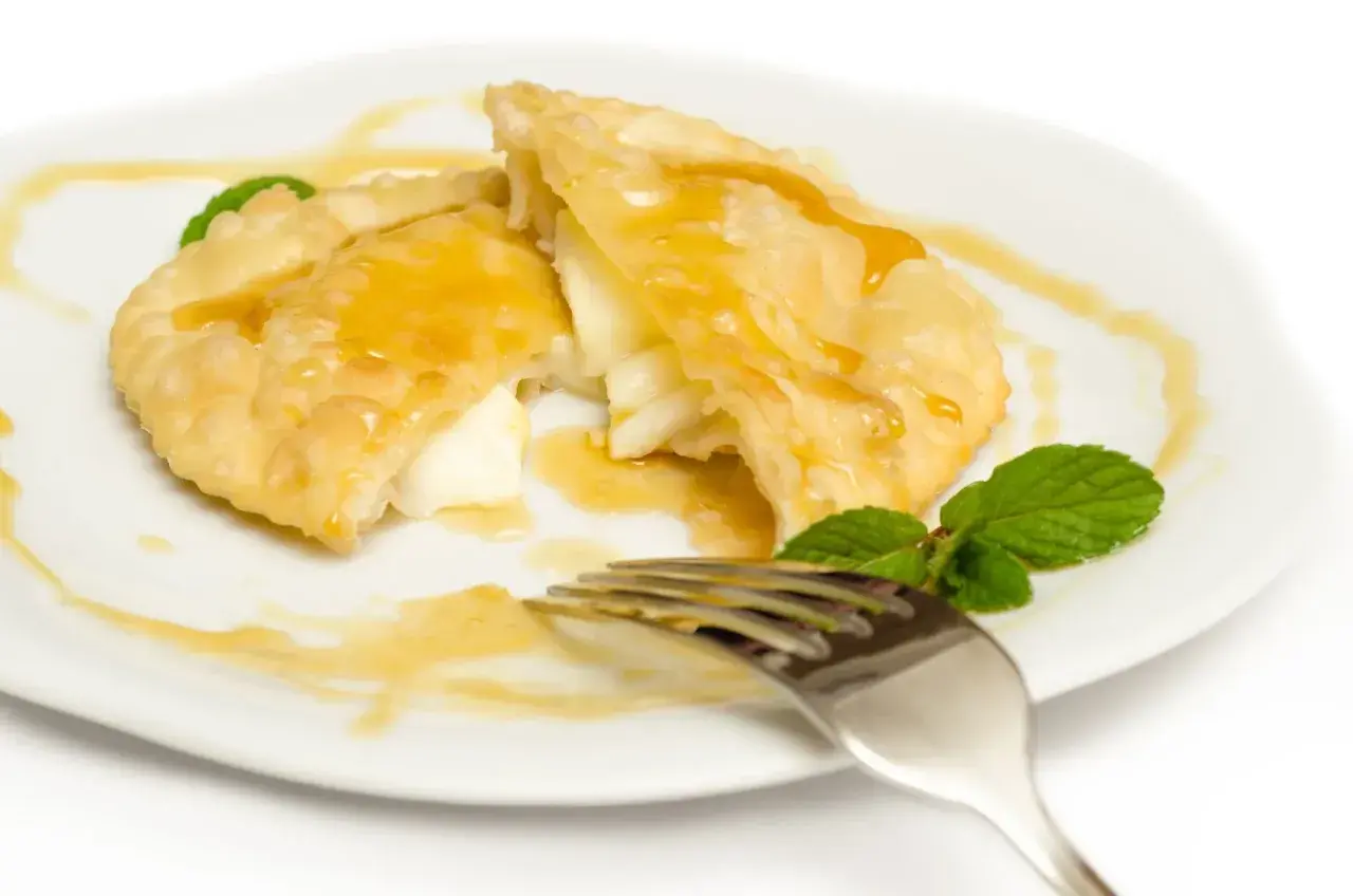 Seadas al miele, un dolce fritto ripieno di formaggio, irrorato di miele dorato e guarnito con menta fresca.
