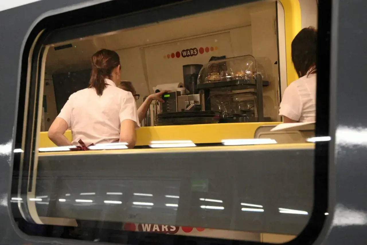 Wnętrze wagonu restauracyjnego z obsługą przygotowującą napoje.