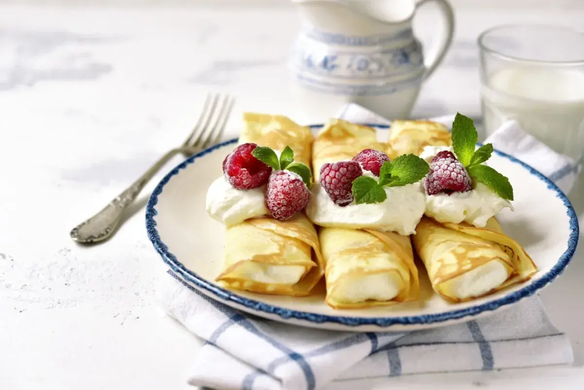 Rolowane naleśniki z mascarpone, ozdobione malinami i miętą, wyglądają apetycznie. Idealne na deser!