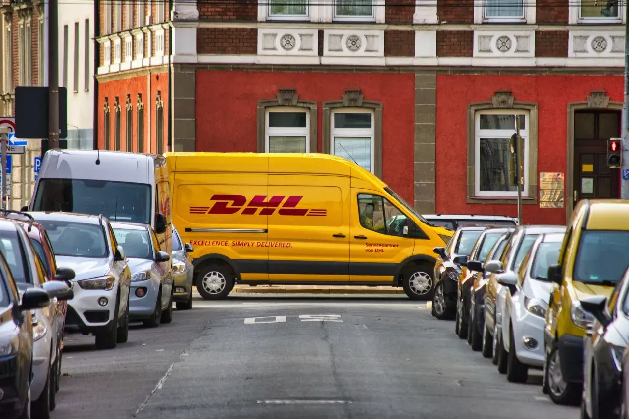 Żółta furgonetka DHL zaparkowana na ulicy, obok inne samochody. Może być potrzebny protokół szkody.