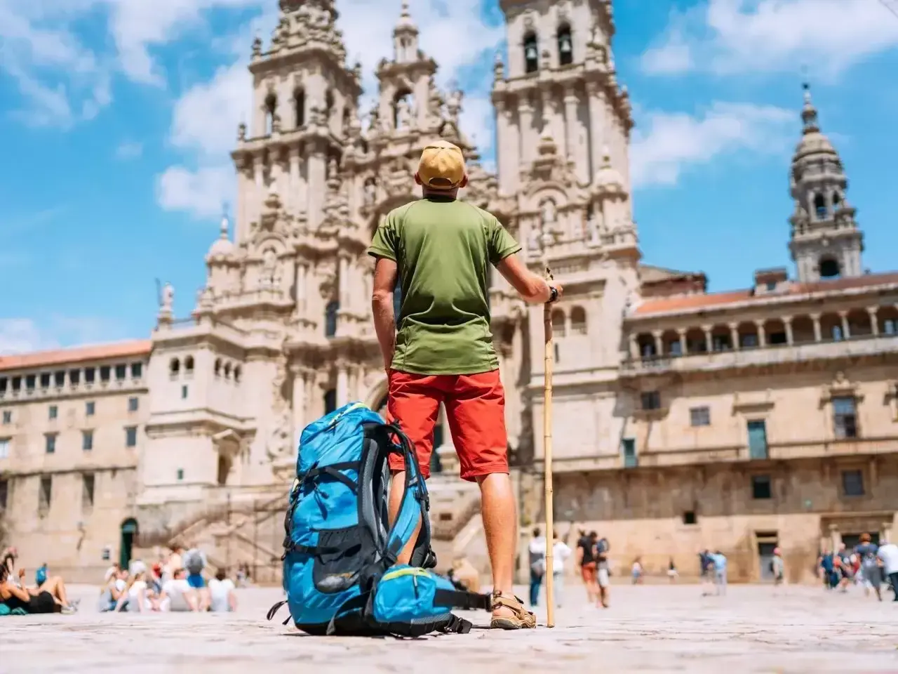 Pielgrzym z plecakiem i laską przed katedrą w Santiago de Compostela. Święta w El Camino to cel podróży.