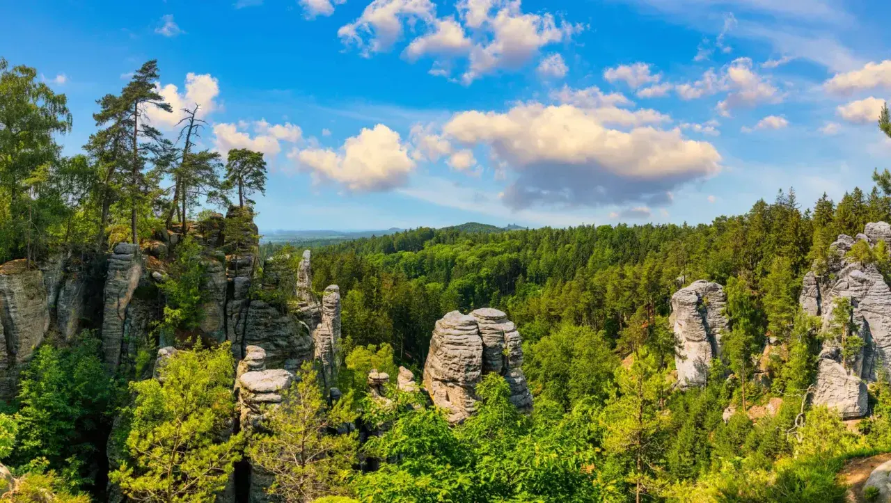 Felsformationen und grüne Wälder laden zum tschechien wandern ein. Ein malerischer Ausblick unter blauem Himmel mit Wolken.