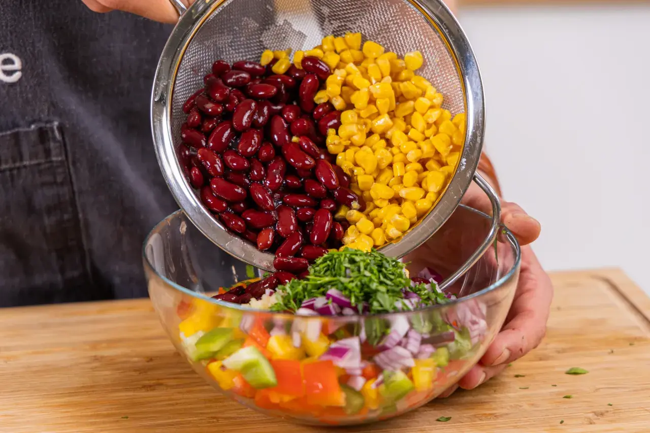 Kidneybohnen und Mais werden in eine Schüssel mit Paprika, Zwiebeln und Kräutern gegeben. Ein bunter Kidneybohnen Salat entsteht.