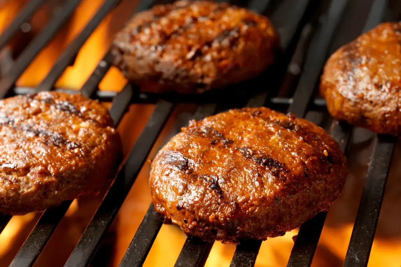 Soczyste burgery z grilla pieką się na rozżarzonych węglach, tworząc apetyczne paski.