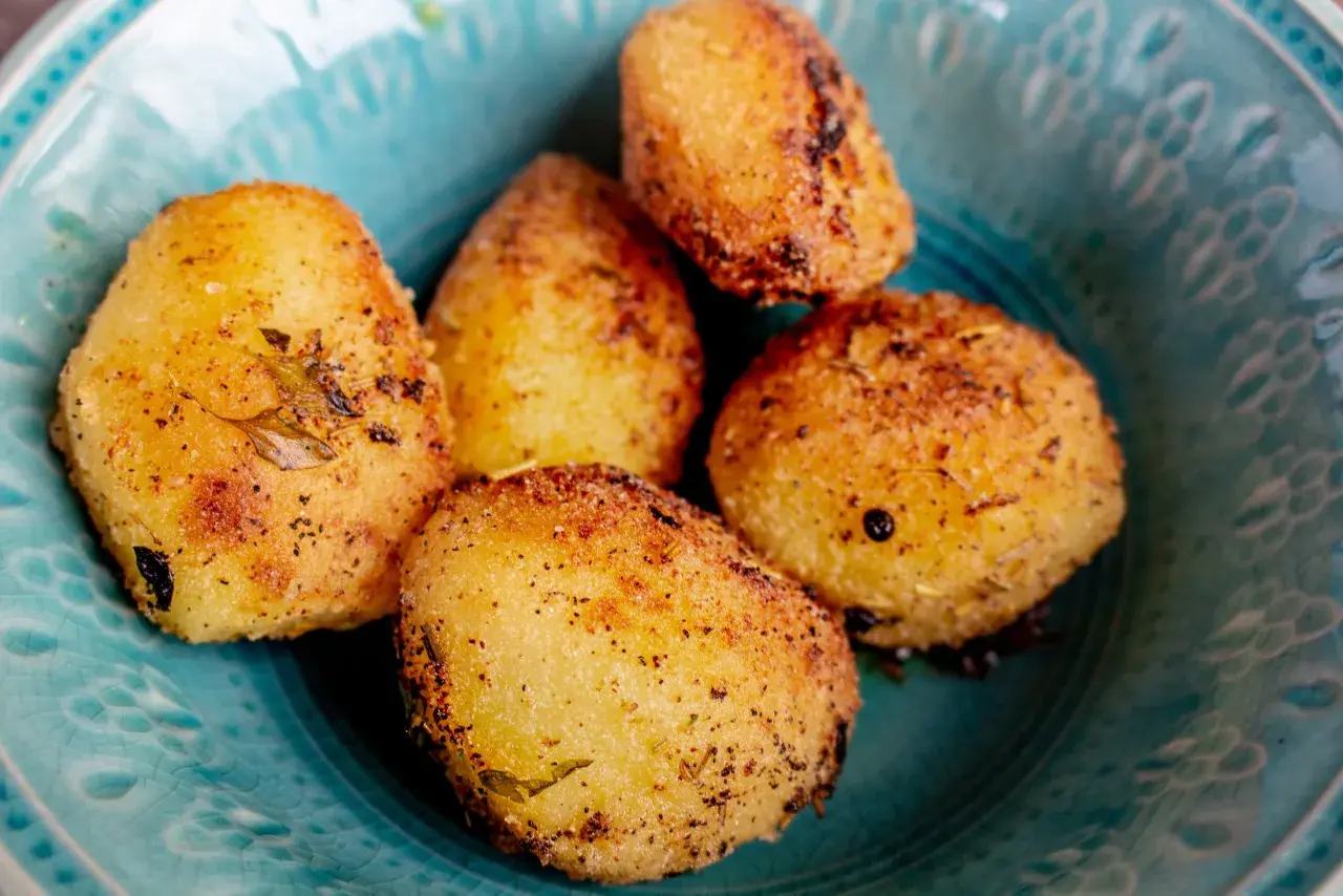 Fem gyllene, rostad potatis i ugn, kryddade med örter och peppar, serveras i en vacker turkos skål.