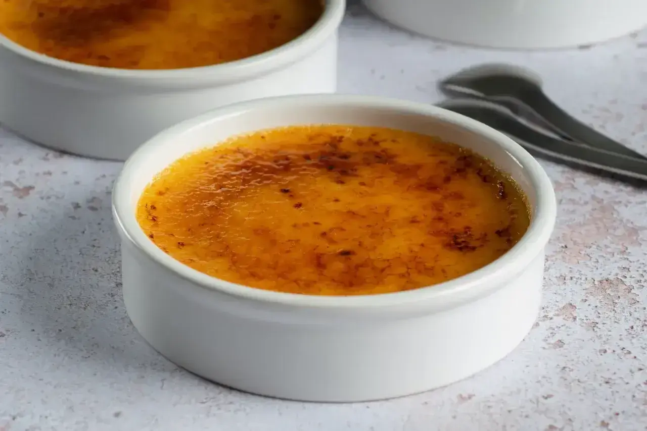 Dwa białe naczynia z pyszną, skarmelizowaną górą. Idealna crema catalana, gotowa do rozkoszowania się.