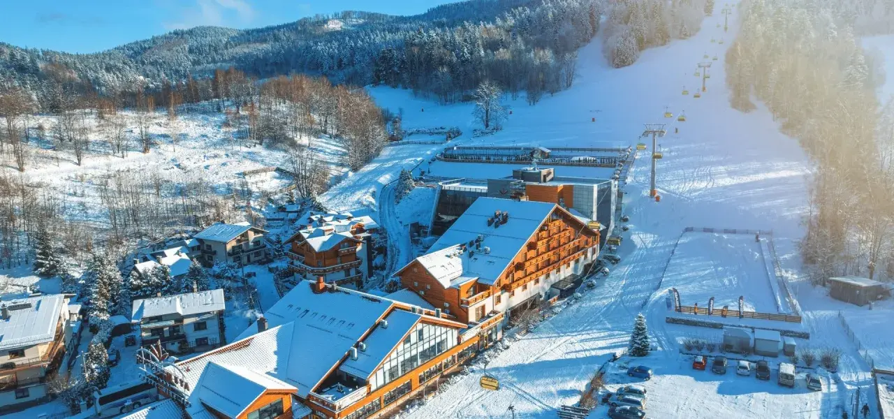 Idealne miejsce na ferie zimowe: ośnieżone góry, hotel z drewnianą elewacją i wyciąg krzesełkowy.