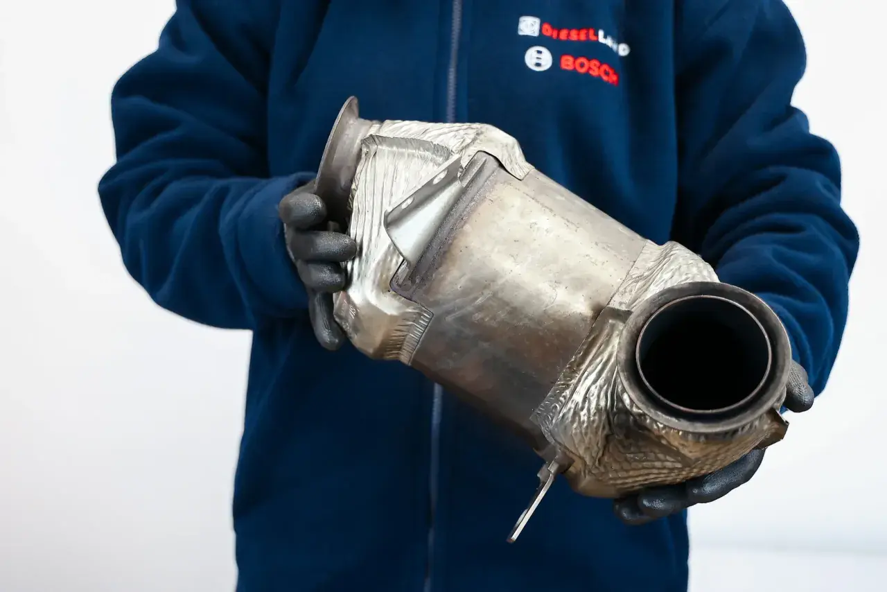 Mechanik w rękawiczkach trzyma filtr DPF. Czy DPF to katalizator? To pytanie często zadawane przez kierowców.