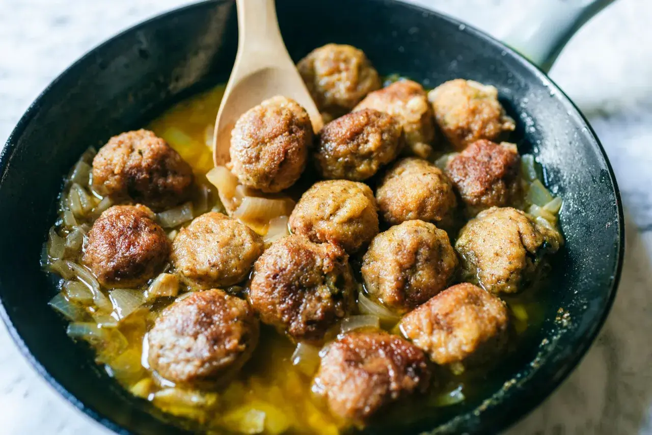 Polpette in bianco dorate e succulente, cotte in padella con cipolle dolci e un sughetto invitante. Un classico confortante.