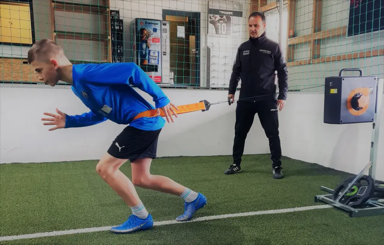 Junge trainiert mit Widerstandsband für schnelles Krafttraining, Coach beobachtet.