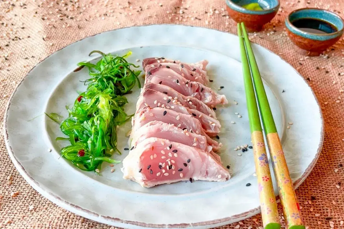 Tataki de bonito, finas lonchas de pescado rosado con semillas de sésamo, acompañadas de ensalada de algas.