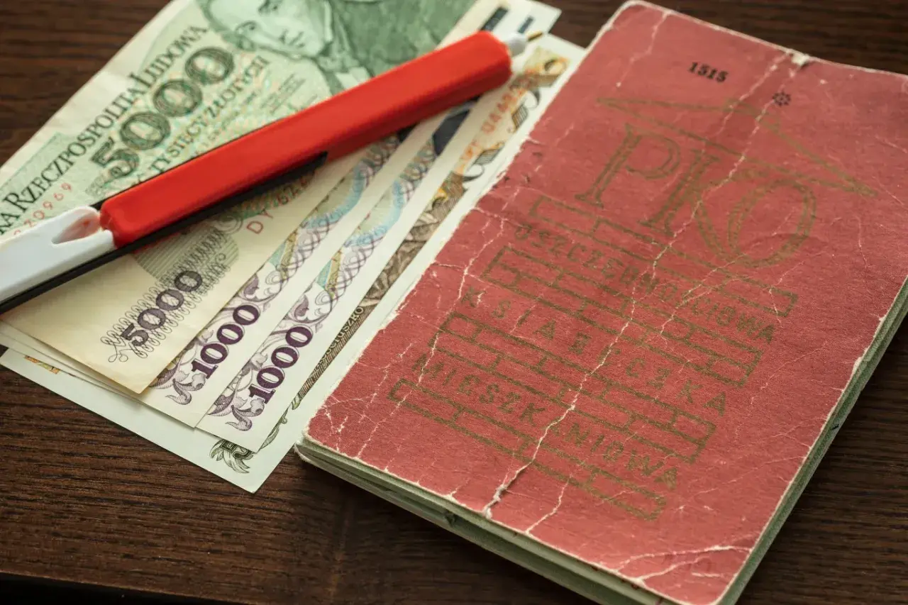 Książeczka mieszkaniowa z PRL-u, banknoty 5000 i 1000 zł oraz czerwony długopis.
