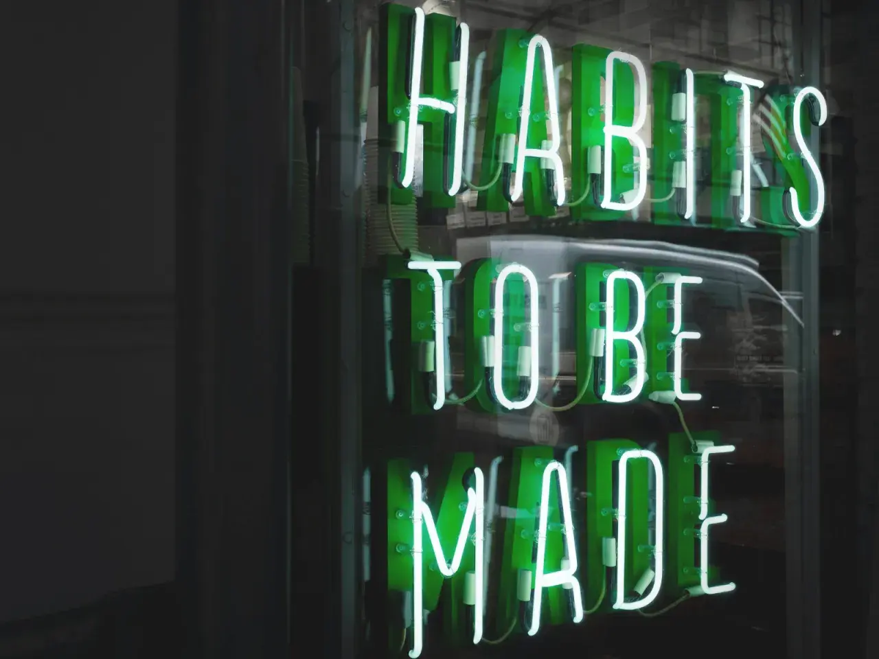 Zielone neony "HABITS TO BE MADE" przypominają o psychologii systemu nagród i kar, który kształtuje nasze nawyki.