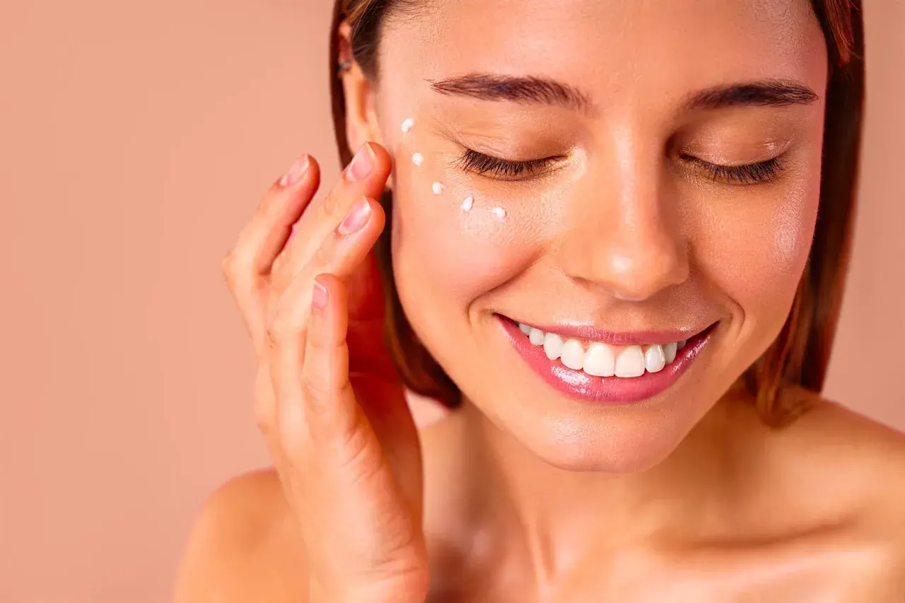 Une femme applique de la crème autour de ses yeux, un geste doux pour un massage des yeux relaxant.
