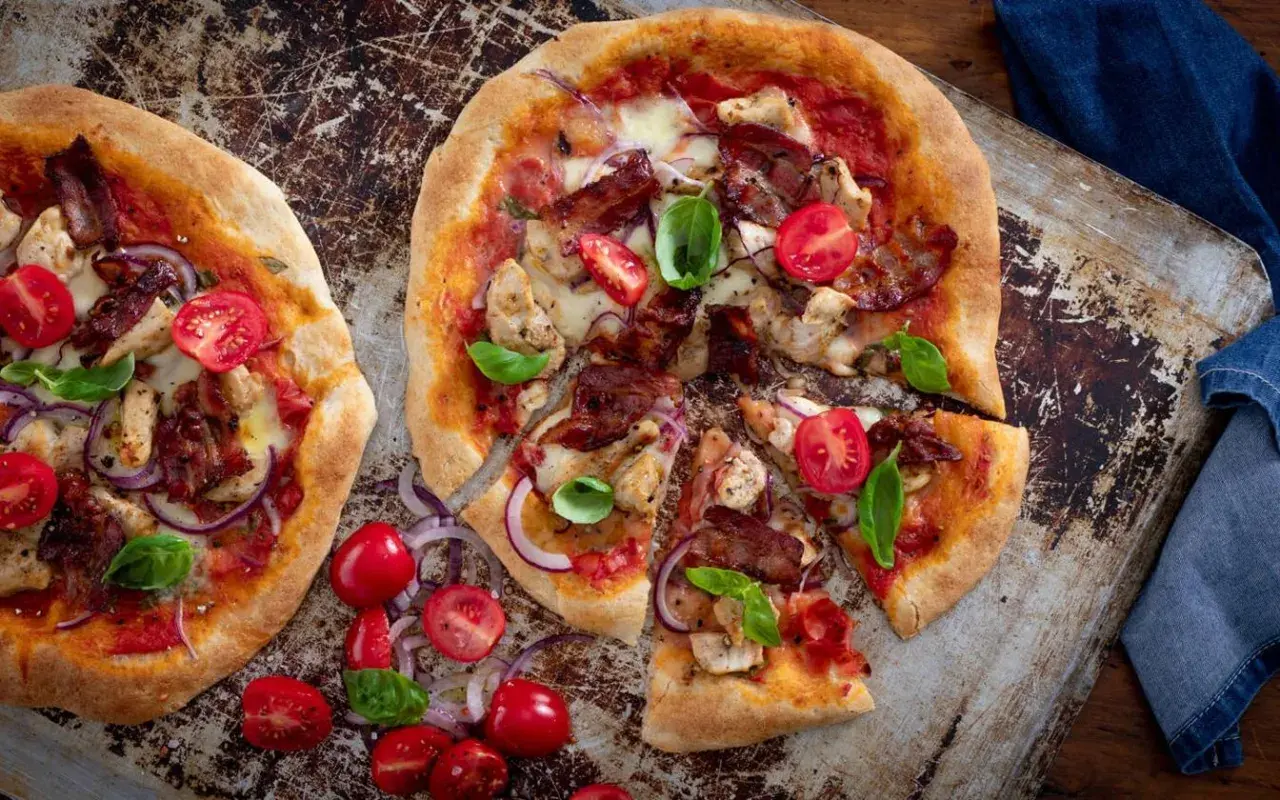 Två läckra pizzor med kyckling och bacon, toppade med körsbärstomater och basilika.