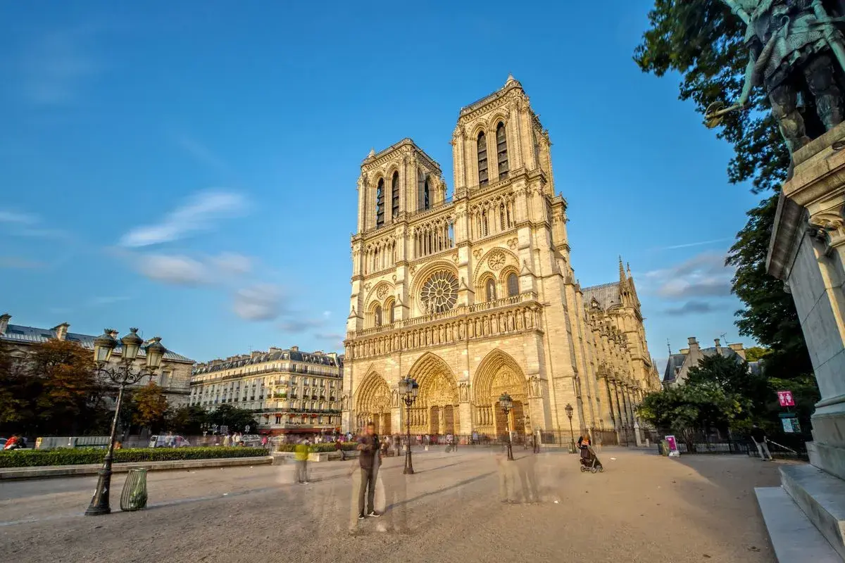 Vue de la cathédrale Notre-Dame de Paris sous un ciel bleu, avec des passants fantomatiques sur le parvis. Un avis sur ce monument emblématique.