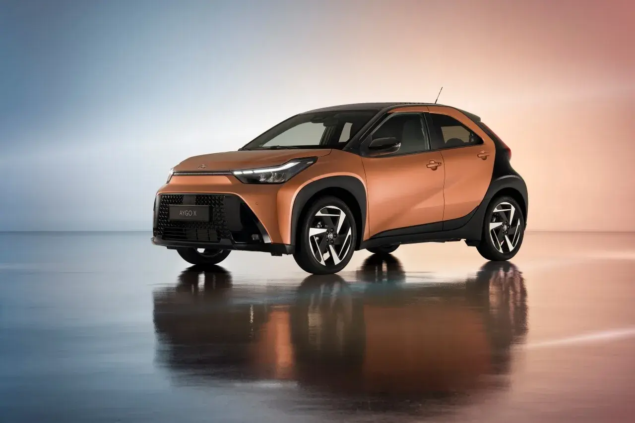 Pomarańczowy Toyota Aygo Cross z czarnymi akcentami i stylowymi felgami, odbijający się w lustrzanej podłodze.