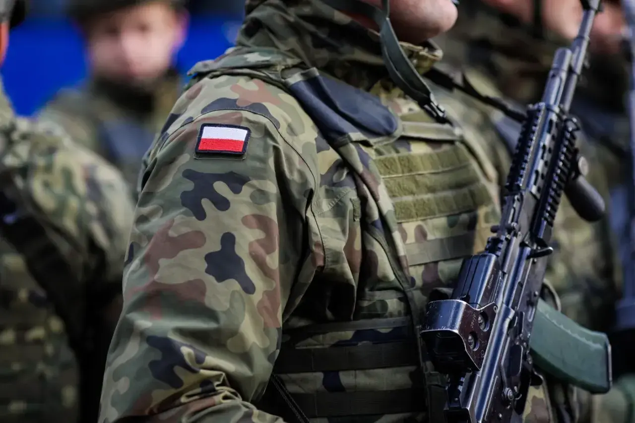 Żołnierze w kamuflażu, z polską flagą na ramieniu, gotowi do mobilizacji. Broń w rękach, czujność na twarzach.