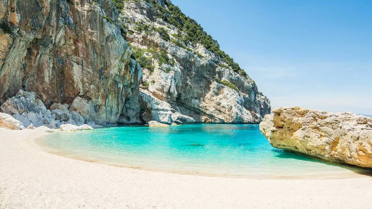 Plage de sable blanc bordée par des falaises imposantes et une eau turquoise cristalline. Un aperçu de ce à quoi ressemble la Riviera italienne.
