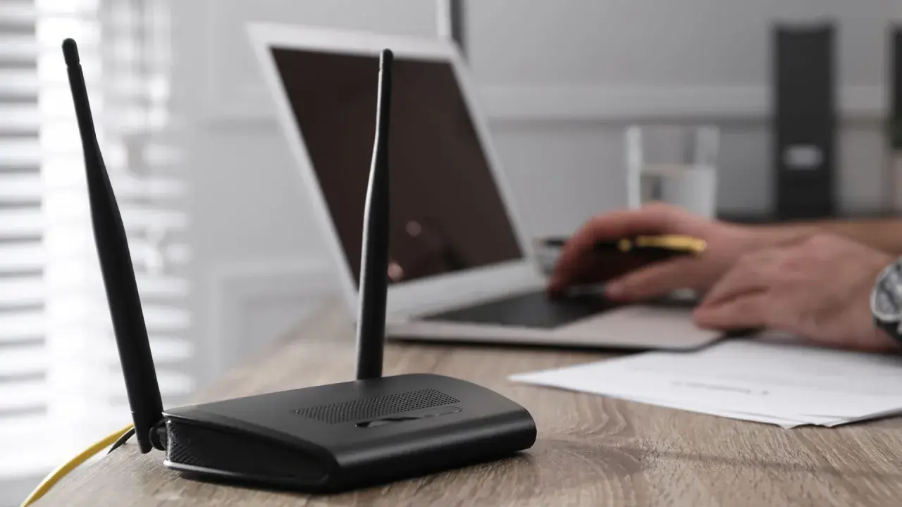 Router mit Antennen steht auf einem Holztisch. Ein Laptop hat kein WLAN mehr, der Nutzer versucht, das Problem zu lösen.