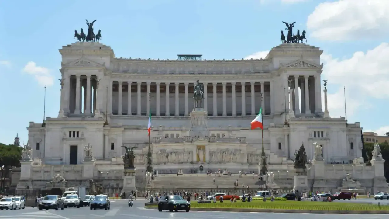 Monumentalny budynek na Piazza Venezia w Rzymie, z rzeźbami i flagami Włoch.
