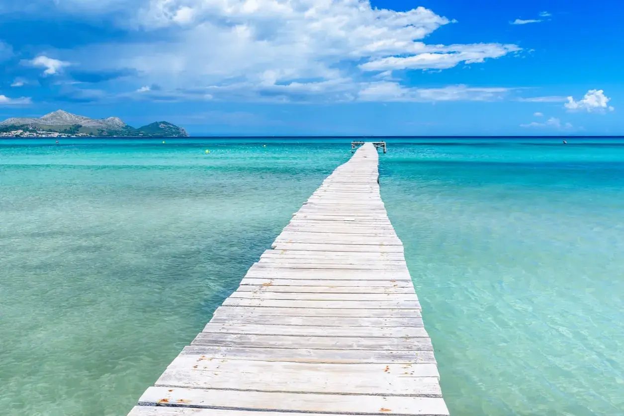 Holzsteg im türkisfarbenen Meer, Berge im Hintergrund. Perfekt für die mallorca beste reisezeit.