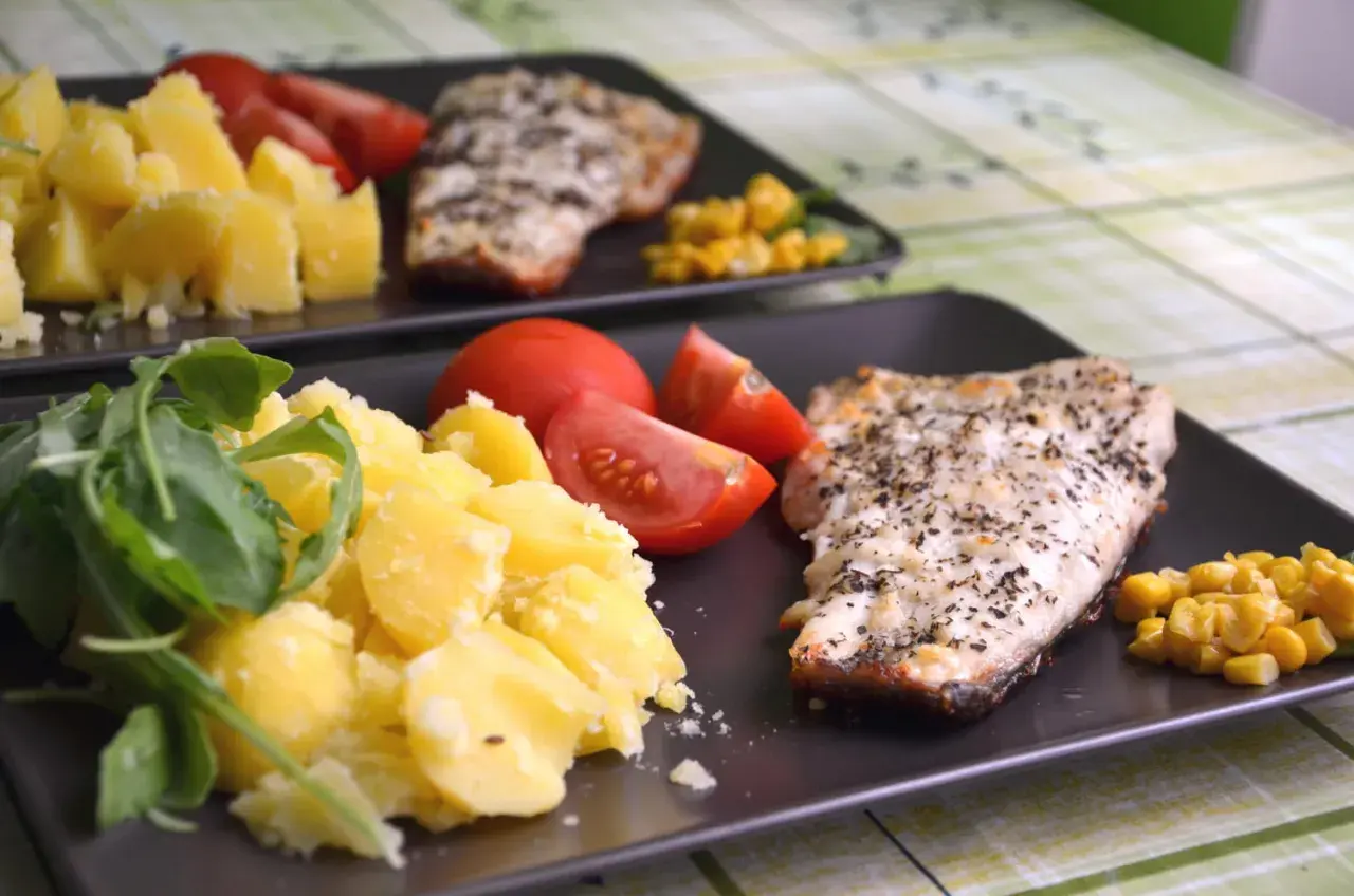 Deux assiettes de poisson grillé avec pommes de terre, tomates et maïs. Un repas sans sucre, sain et savoureux.