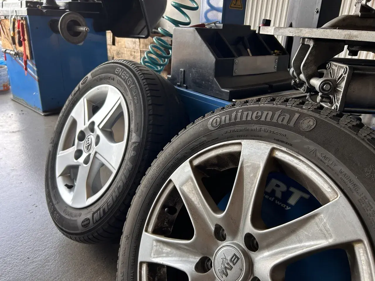 Dwa aluminiowe felgi z oponami Continental i Michelin, gotowe do prostowania felgi aluminiowej w warsztacie.