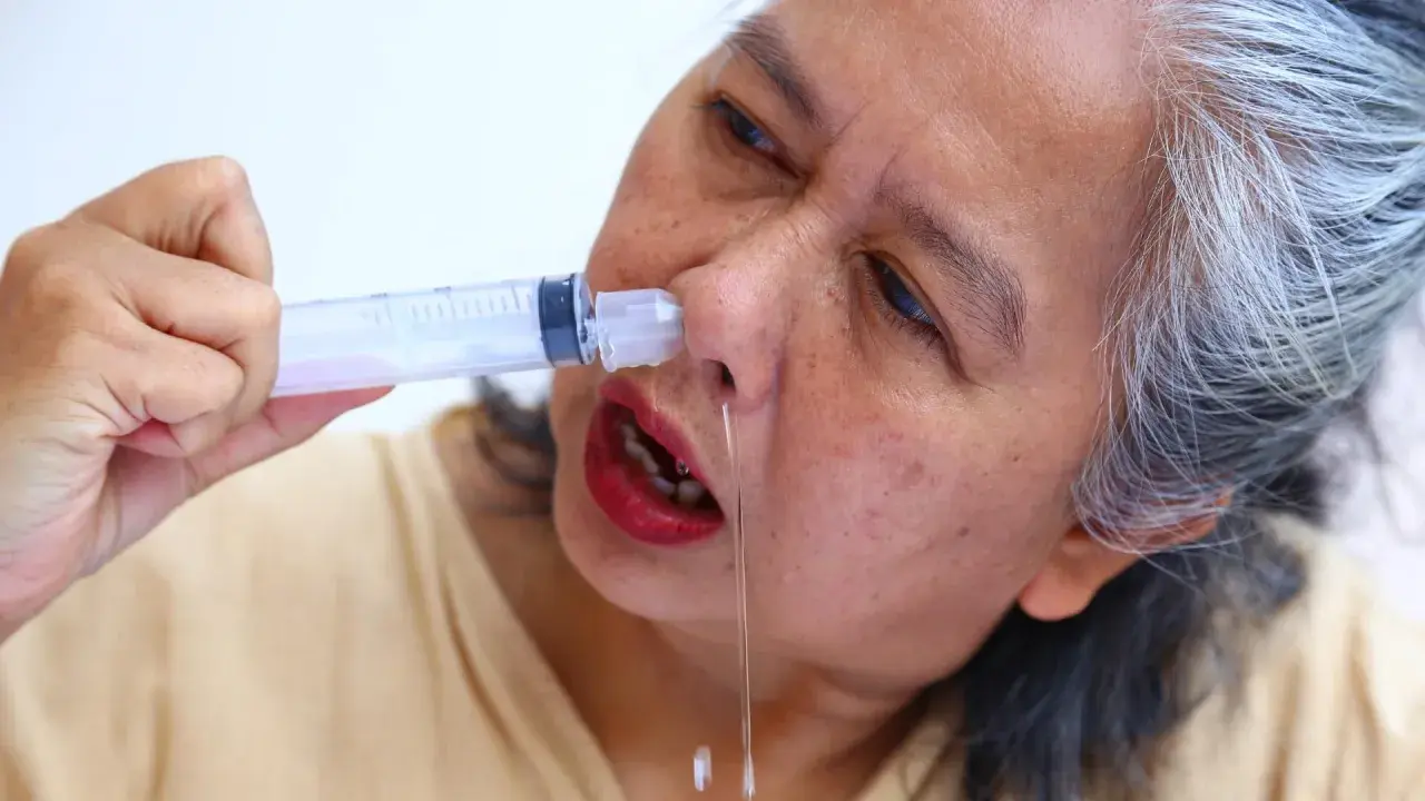 Mujer mayor realizándose lavados nasales con jeringa. Alivio para la congestión nasal en adultos.