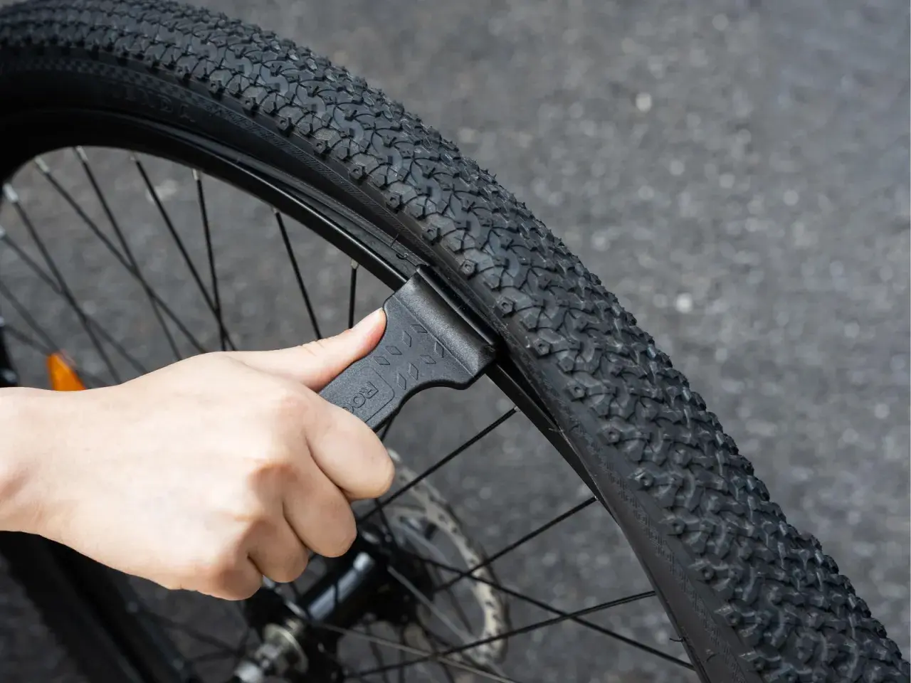 Dłoń używa czarnej łyżki do opon rowerowych, aby zdjąć oponę z obręczy. To pokazuje, jakie łyżki do opon rowerowych są potrzebne do naprawy.
