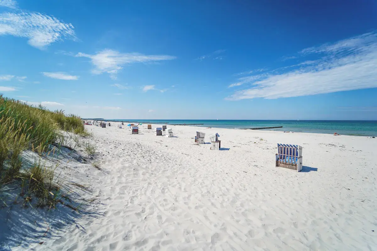 Ein sonniger Hiddensee Strand mit vielen Strandkörben, feinem Sand und dem blauen Meer.