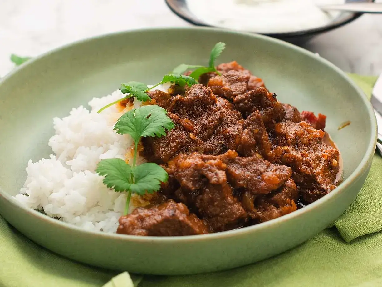 A bowl of lamb curry with rice and cilantro garnish.