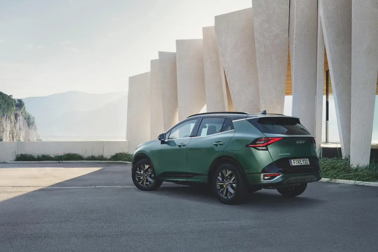 Zielony samochód Kia Sportage zaparkowany przed nowoczesnym budynkiem z elementami skalnymi w tle.