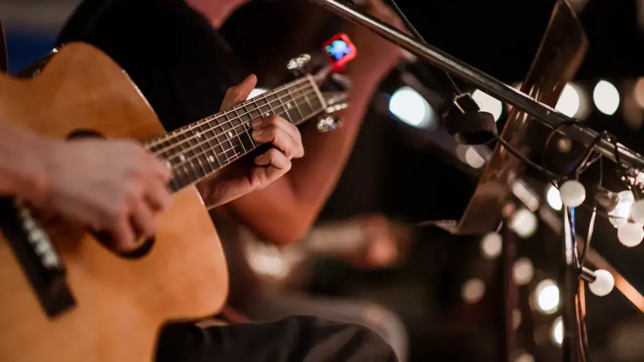 Ręce grające na gitarze akustycznej, w tle migoczą światła, tworząc atmosferę jak na stena line dyskotece.