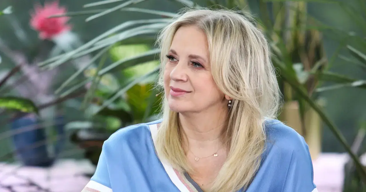 Marzena Rogalska w błękitnej bluzce z naszyjnikiem, na tle zieleni.