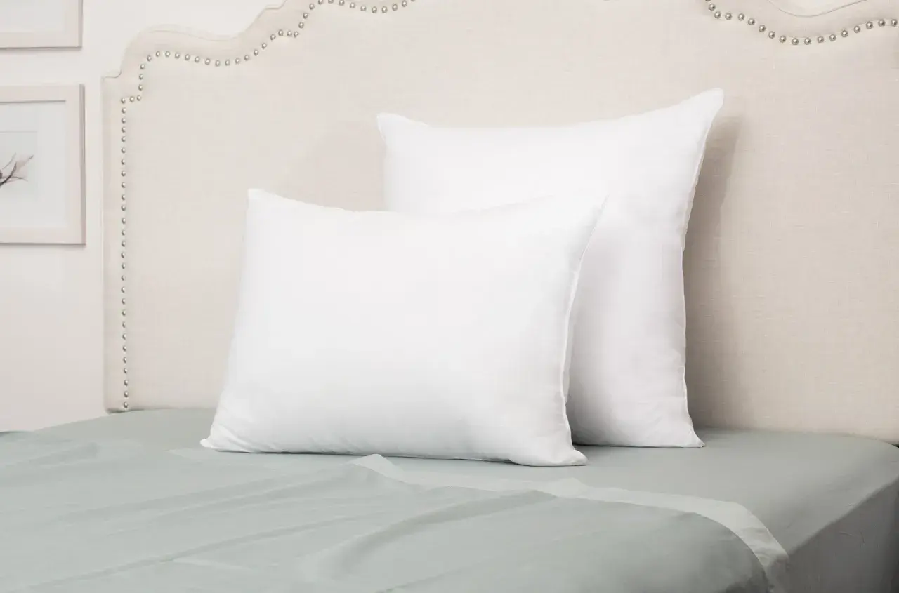 Two white pillows on a bed. The front pillow is a euro sham, while the larger one behind it is a standard sham, showcasing their size difference.