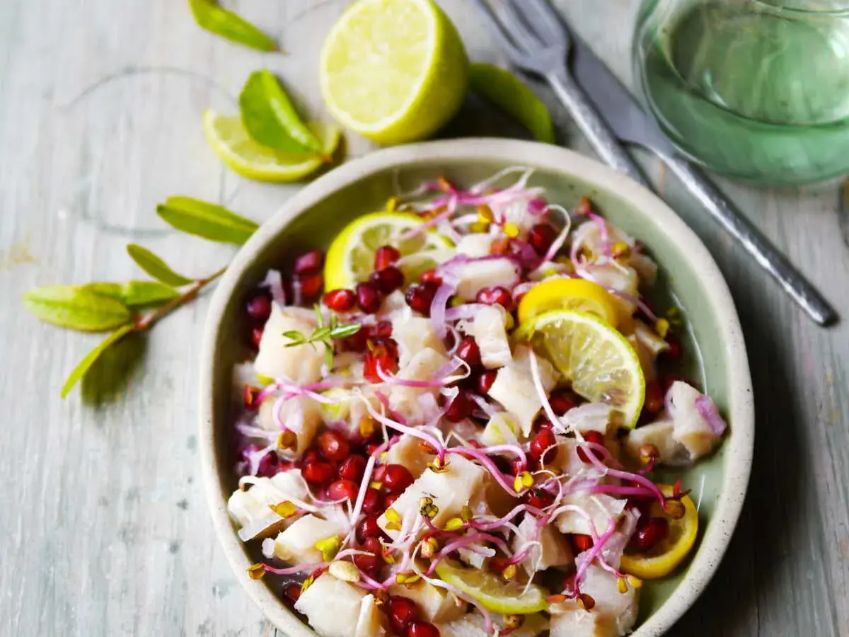 Un délicieux ceviche de poisson frais, garni de grenade, de pousses et de rondelles de citron vert.