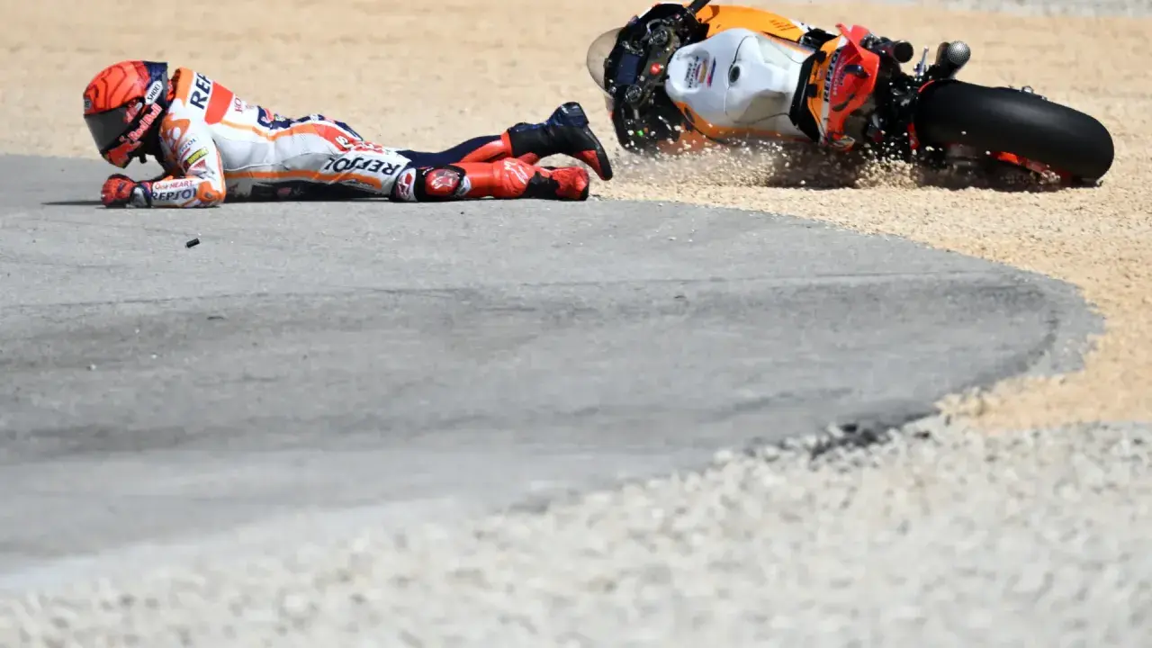 Piloto de MotoGP en el suelo tras una caída. La moto, volcada, derrapa en la grava. Un largo lap de competición que terminó mal.