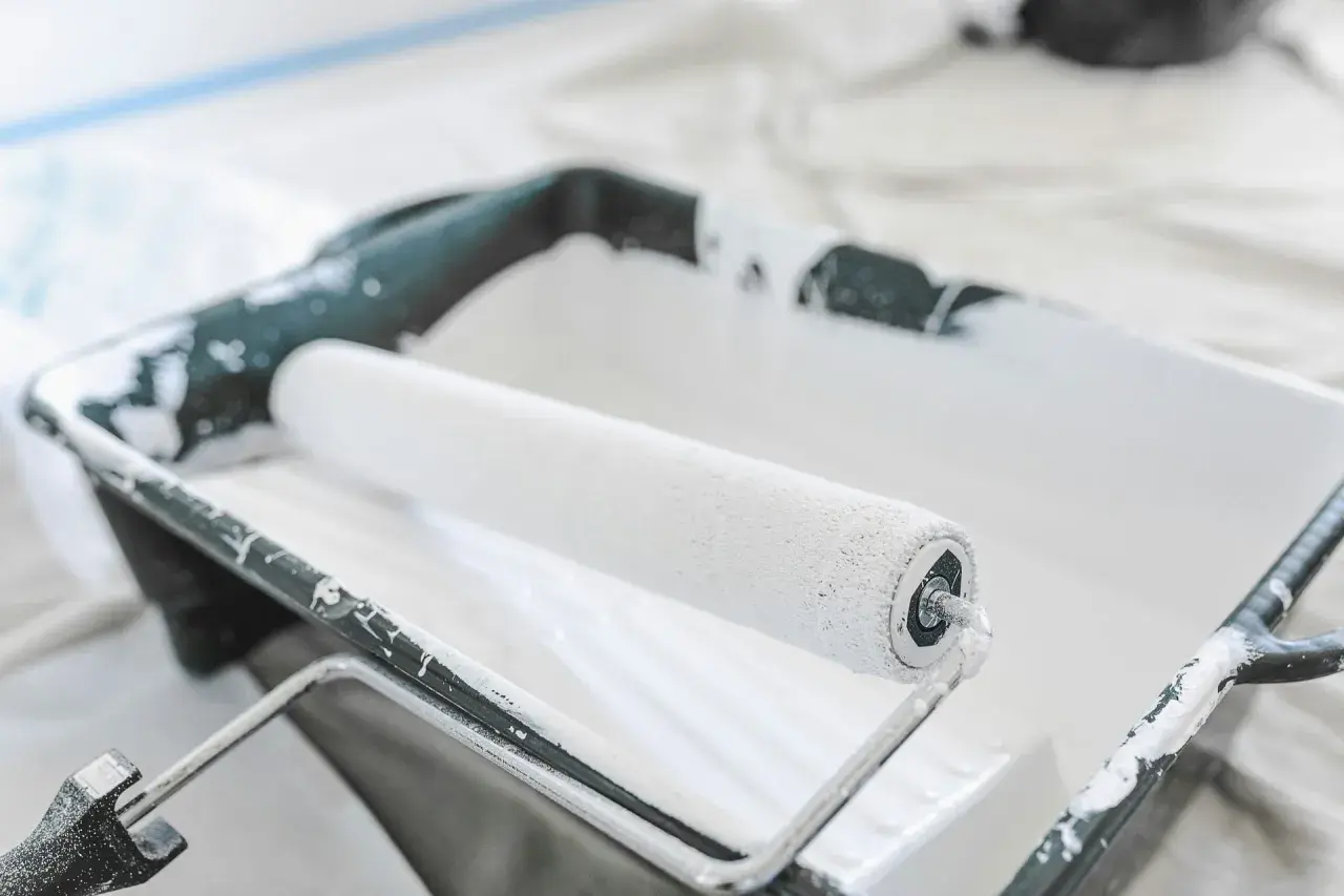 Un rouleau à peinture blanc est posé dans un bac en plastique noir, prêt à enlever la peinture.